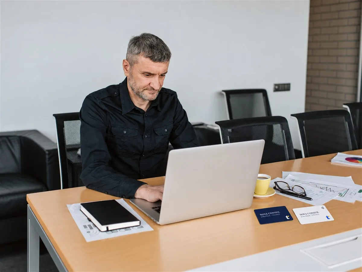 Homme travaillant sur un ordinateur portable, deux cartes de visite NFC posées sur la table